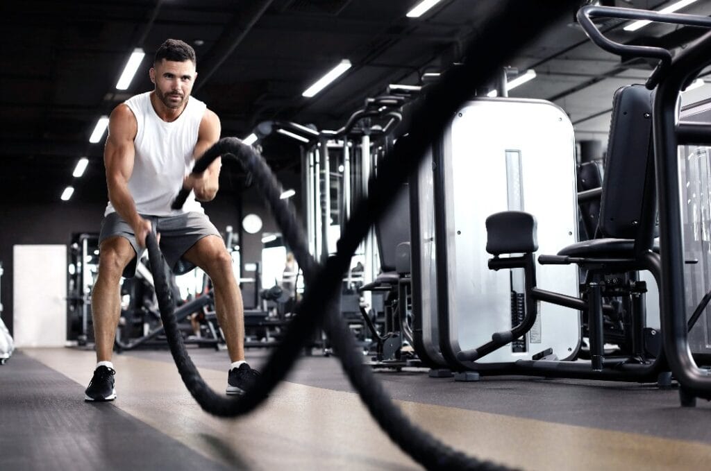 Athletic young man with battle rope doing exercise in functional training fitness gym.